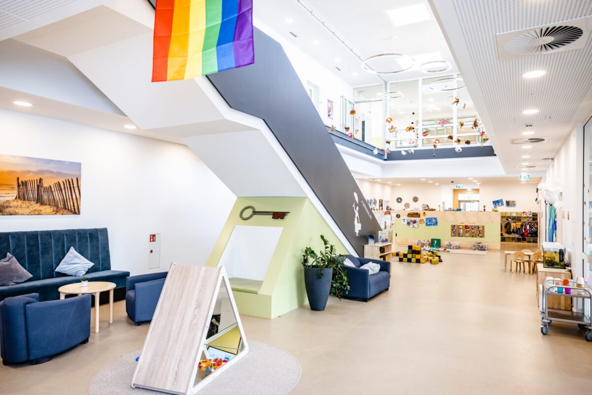 Kita Landwehr in Osnabrück Bunt dekorierte Kita mit Spielbereichen und einem großen Treppenaufgang; eine Regenbogenflagge hängt von der Decke.