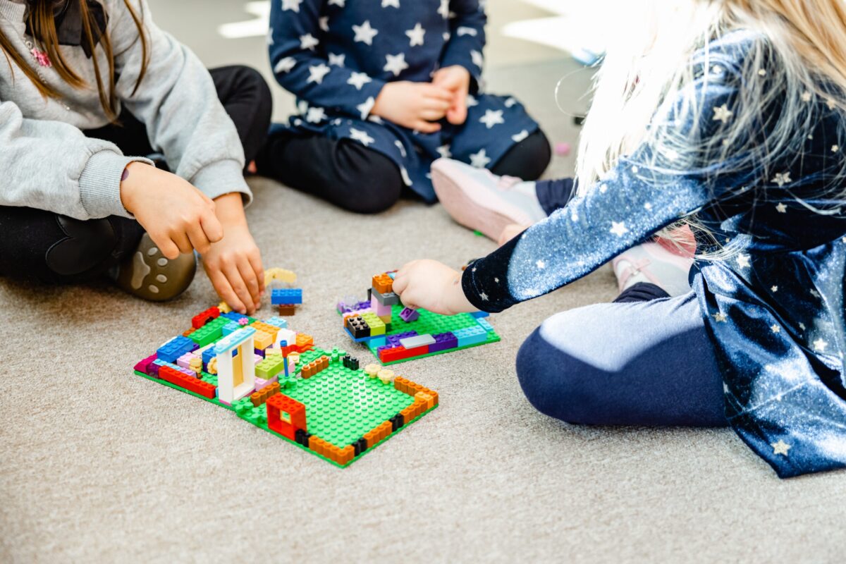 Bunte Bauklötze im Spiel Kinder spielen mit bunten Bauklötzen auf dem Teppich; eine Hand fügt Teile hinzu, während andere Hände ebenfalls am Spiel beteiligt sind.